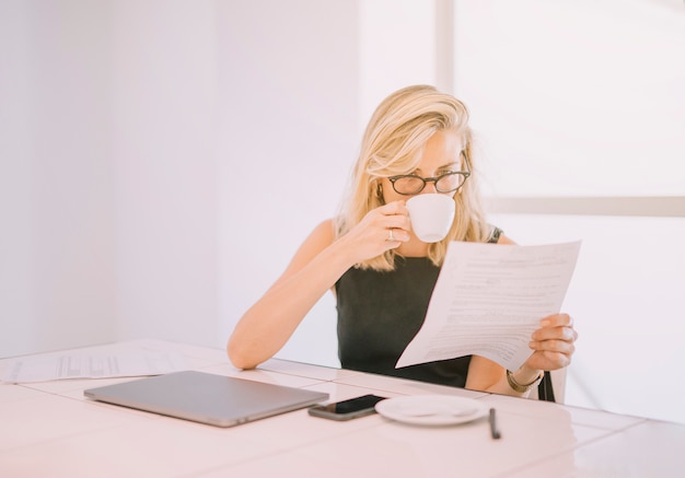 Young businesswoman drinking coffee while reading the document in the office