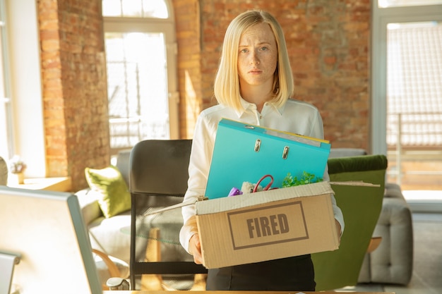 Free photo young businesswoman fired, looks upset. has to pack her office belongings and to leave work place for new worker. problems in occupation, stress, unemployment, new way of life or end of career.