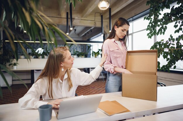 Young businesswoman holding box of personal belongings about to leave office after quitting job