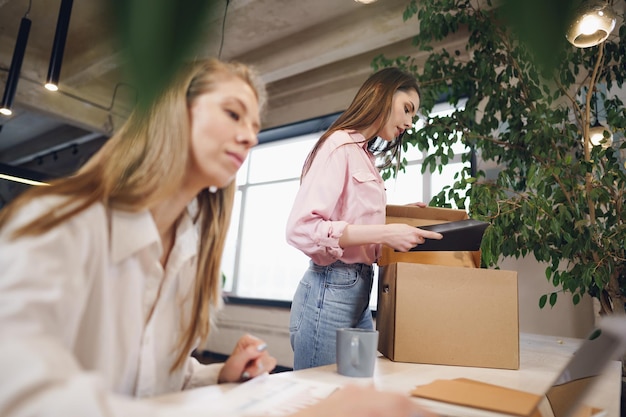 Young businesswoman holding box of personal belongings about to leave office after quitting job