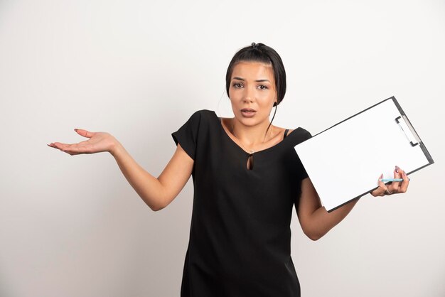 Young businesswoman holding clipboard on white wall.