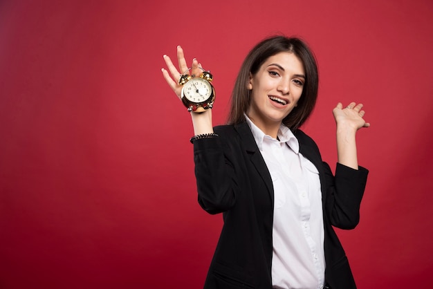 Young businesswoman holding clock on red background. 
