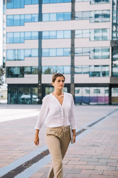 Young businesswoman holding laptop in hand walking at office campus