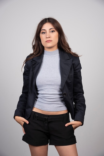 Young businesswoman in jacket standing and posing over a gray wall. 