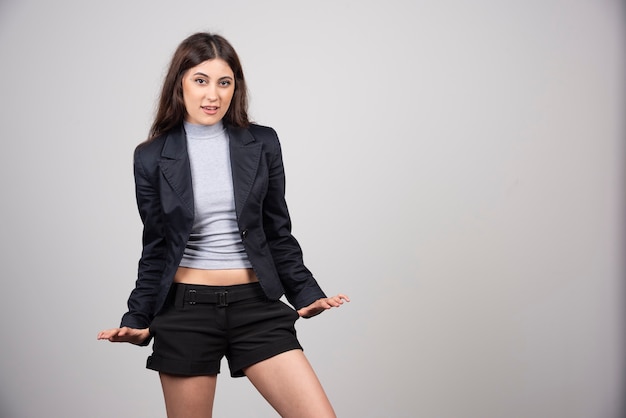 Young businesswoman in jacket standing and posing over a gray wall. 