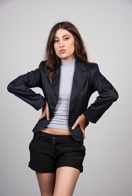 Young businesswoman in jacket standing and posing over a gray wall. 