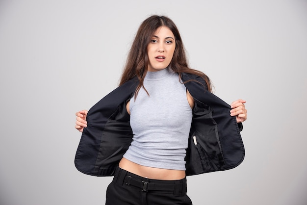 Young businesswoman in jacket standing and posing over a gray wall. 