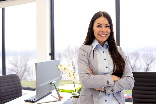 Young businesswoman leaning on her working desk with crossed arms