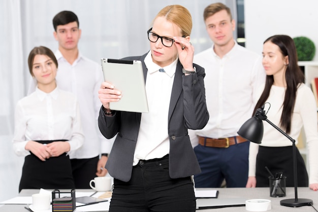 Young businesswoman looking at digital tablet standing in front of business people in office