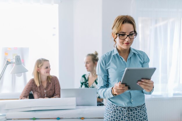 Young businesswoman looking at digital tablet standing in front of her colleagues at office