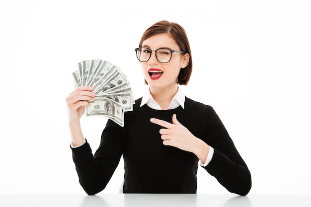 Free photo young businesswoman pointing with finger at money and winking