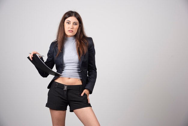 A young businesswoman posing with document on clipboard isolated on gray wall. 