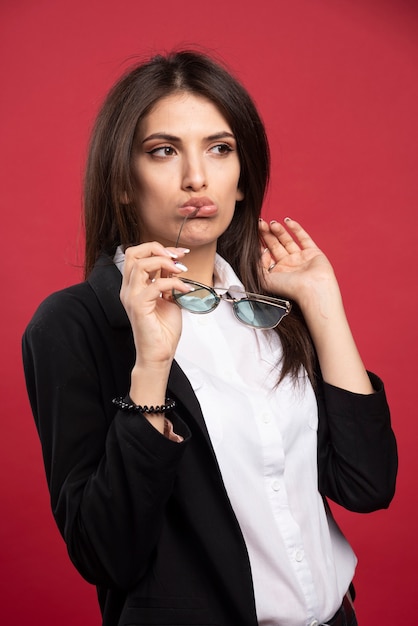Young businesswoman posing with glasses on red background. 