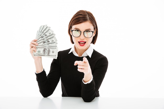 Young businesswoman showing money and pointing with finger