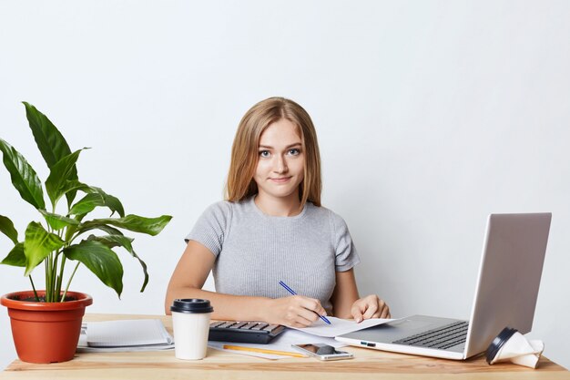 Young businesswoman signing documents while sitting at table at her workplace