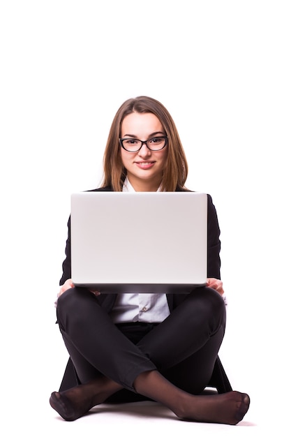 Young businesswoman sitting on floor and using laptop isolated on white wall