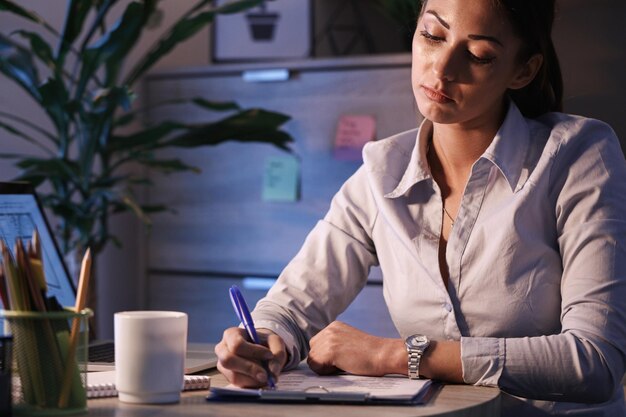 Young businesswoman sitting at office desk and filling documents while going through paperwork