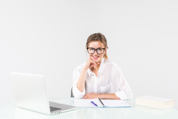 Young businesswoman sitting at a office table with laptop, looking at the camera isolated on white background