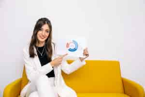 Free photo young businesswoman sitting on yellow sofa showing graph