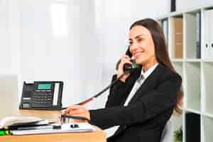 Foto gratuita giovane donna di affari che sorride mentre parlando sul telefono nell'ufficio