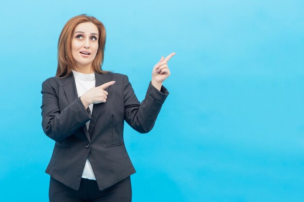 Young businesswoman standing on blue background and point fingers to the side