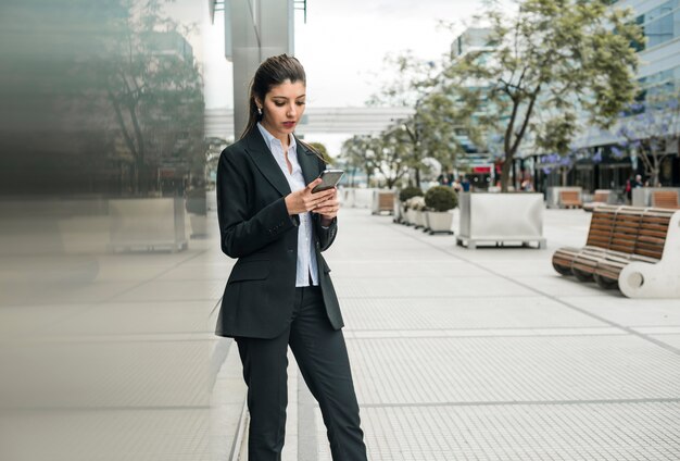 Young businesswoman standing at business campus using mobile phone