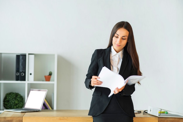 Free photo young businesswoman standing in front of office desk reading documents