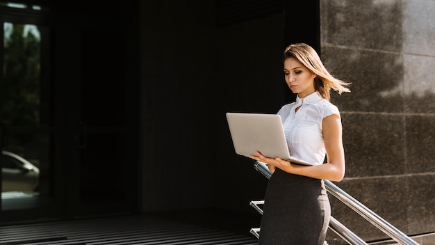 Young businesswoman standing near the railing looking at laptop