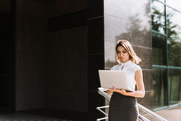 Young businesswoman standing outside the office using laptop