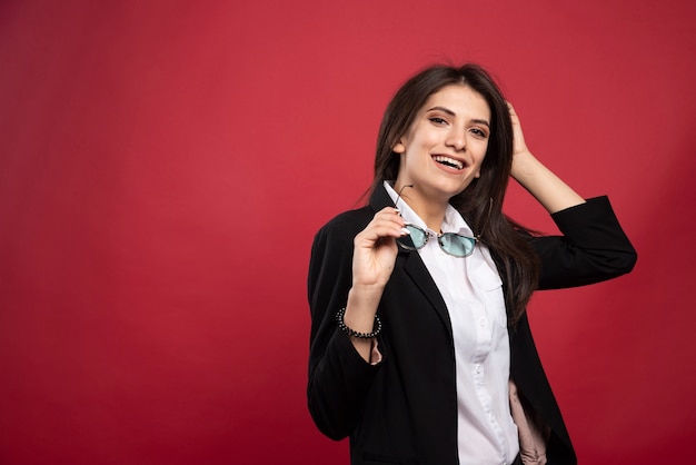 Young businesswoman standing with glasses on red background. 