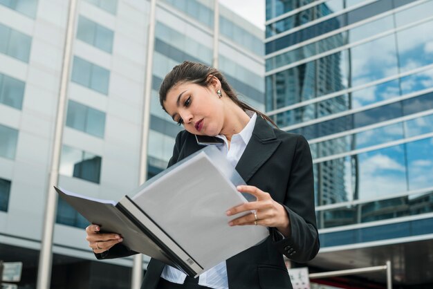Young businesswoman talking on mobile phone looking at folder