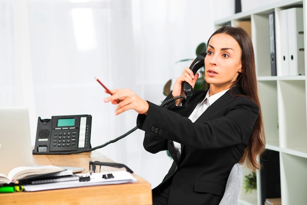 Free photo young businesswoman talking on telephone pointing pencil at somewhere