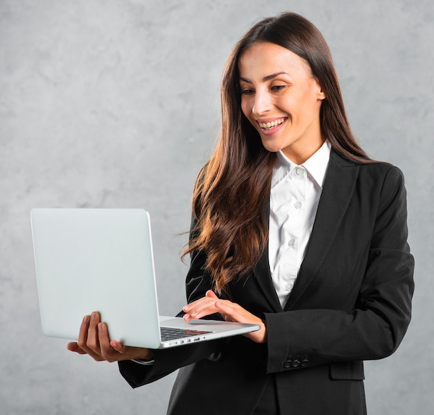 Young businesswoman typing on laptop standing against gray background