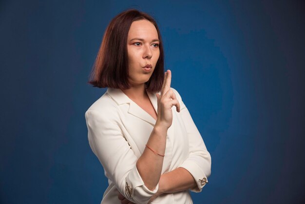 Young businesswoman in white blazer blowing gun. 