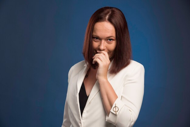 Young businesswoman in white blazer smiling secretly. 