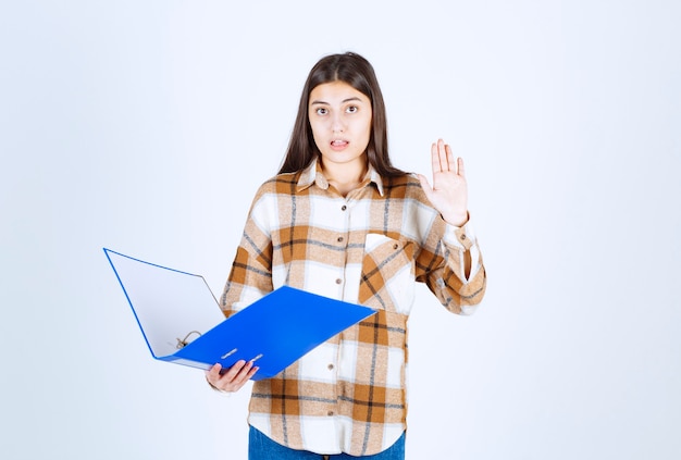 Young businesswoman with blue holder standing on white wall. 