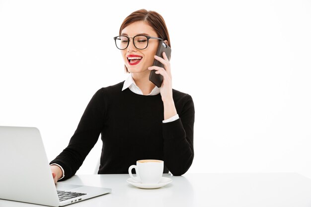 Young businesswoman with coffee or tea cup and laptop computer, talking by phone