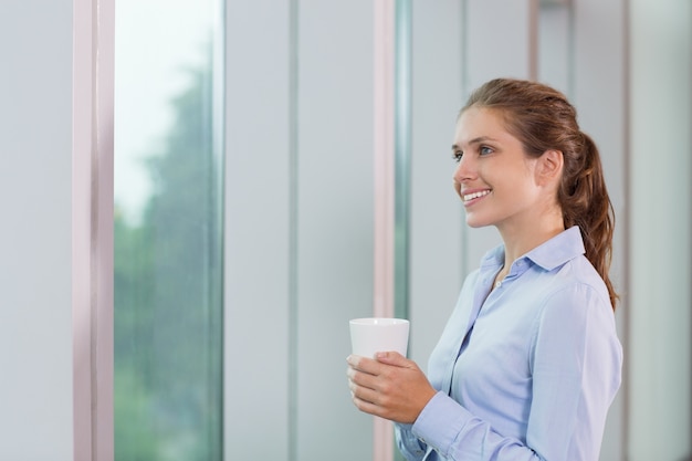 Young Businesswoman with Cup at Window