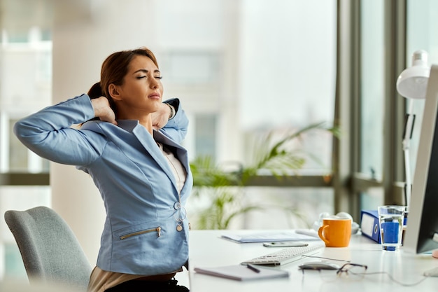 Free photo young businesswoman with eyes closed stretching while working at her office desk