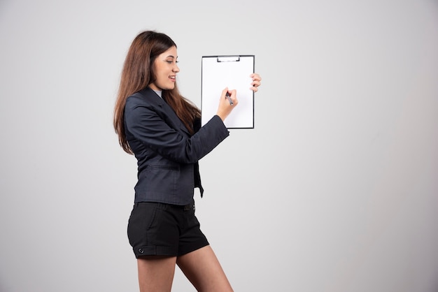 A young businesswoman writing in clipboard isolated on gray wall. 