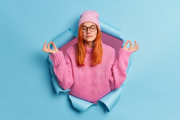 Foto gratuita la giovane donna calma e rilassata tiene le mani nel gesto di yoga tiene gli occhi chiusi medita al coperto respira profondamente medita al coperto.