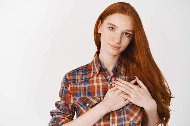 Free photo young caring and heartfelt woman holding hands on heart, thanking for something, standing over white wall