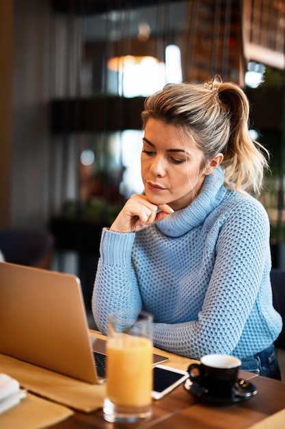 Молодая деловая женщина, держащая руку на подбородке, работает за компьютером и думает о перерыве на кофе