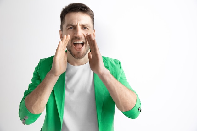 Young casual man shouting. Shout. Crying emotional man screaming on studio background. male half-length portrait. Human emotions, facial expression concept.