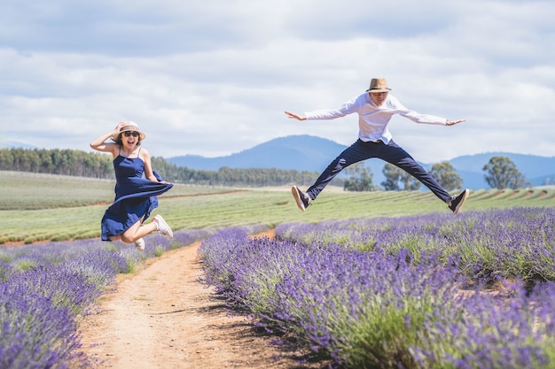 Young casual trendy boy and girl jumping at lavender field. Blue cloud summer daytime.