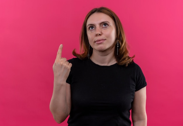 Young casual woman pointing and looking up on isolated pink wall with copy space