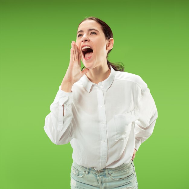Young casual woman shouting. Shout. Crying emotional woman screaming on green studio background. Female half-length portrait.
