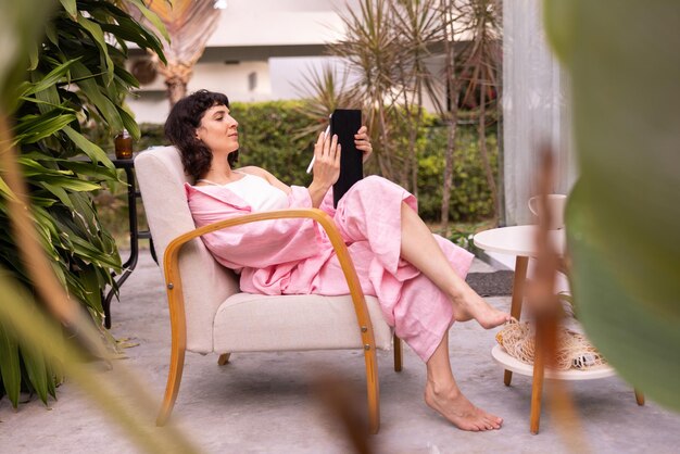 Young caucasian artist brunette girl in pink clothes makes sketches in tablet sitting on chair in backyard Hobby and pleasure concept