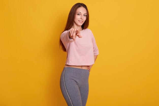 young Caucasian athletic girl pointing, wearing stylish sporty clothing, model posing isolated on yellow .Fitness and sport concept.