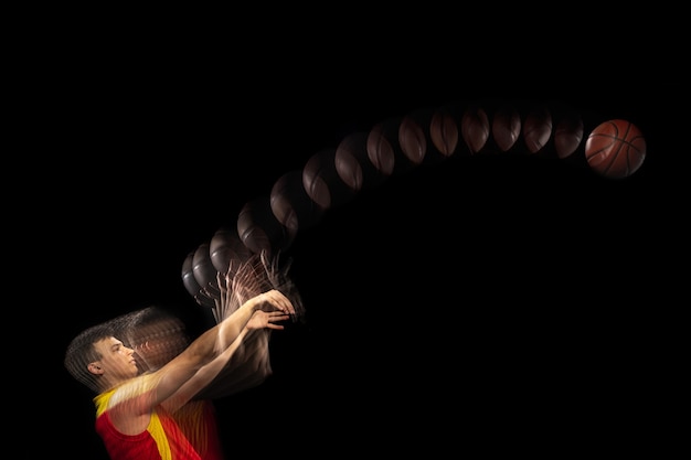 Young caucasian basketball player in motion and action in mixed light on dark background.